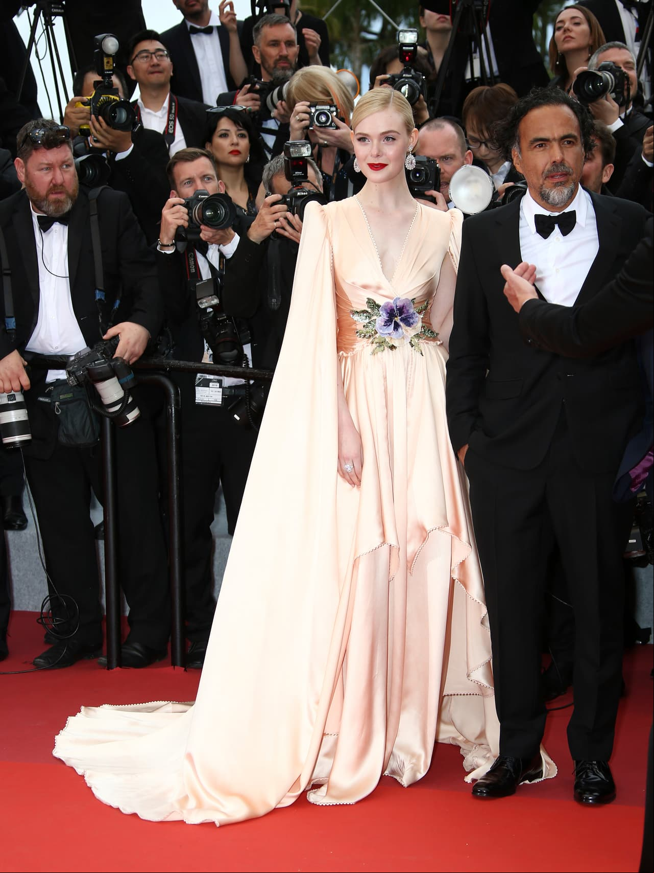 Acompañada del director mexicano, Alejandro González Inarritu, la actriz Elle Faning desfiló por la alfombra luciendo un vestido amarillo con capa, escote en V y flores con lentejuelas a la cintura, todo de la firma Gucci.