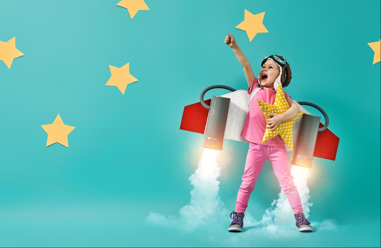 Little child in an astronaut costume is playing and dreaming of becoming a spaceman. Portrait of funny kid on a background of bright blue wall.
