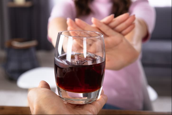 Close-up Of A Woman's Hand Refusing Glass Of Drink Offered By Person