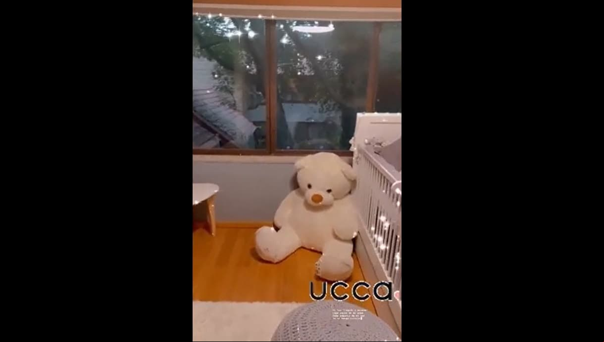 Un peluche gigante en forma de oso reposa al pie de la cuna, mientras que un puff en color gris decora la otra esquina.