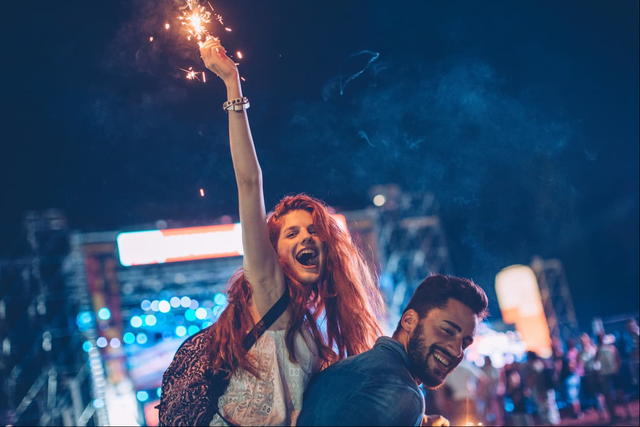 A young couple embracing at an outdoors music festival. They holding sparklers in summer night.